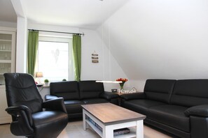 Ein Wohnzimmer mit einem schwarzen Ledersofa, einem Holztisch und einem grünen Vorhang.