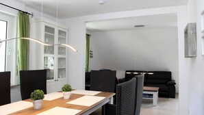 A modern living room with a dining area, featuring a wooden table, black chairs, a black sofa, and a glass cabinet. - Holiday Apartment “Olsberg” with Mountain View, Private Terrace and Wi-Fi (Olsberg)