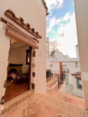 Un estrecho callejón con la entrada de un edificio, un muro de piedra y una escalera que lleva a un balcón en un segundo piso.