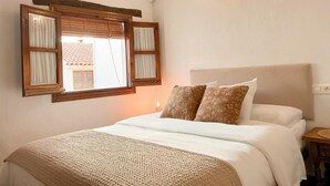Een slaapkamer met een bed, een raam met luiken, een hoofdbord en een wandlamp.