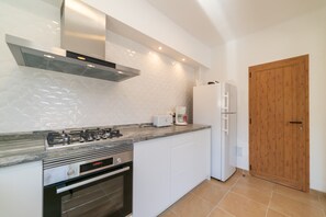 Eine Küche mit Gasherd, Backofen, weißen Schränken, einem Kühlschrank und einer Holztür.