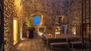 Une cour intérieure aux murs de pierre, une table en bois avec des bancs et des plantes en pot.