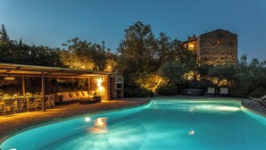 Une piscine dotée d’un espace salon aménagé en contrebas et, en arrière-plan, un bâtiment en pierre.