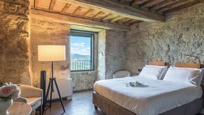 Une chambre à coucher avec un grand lit, une table de chevet, une lampe et une vue sur l’extérieur par une fenêtre.