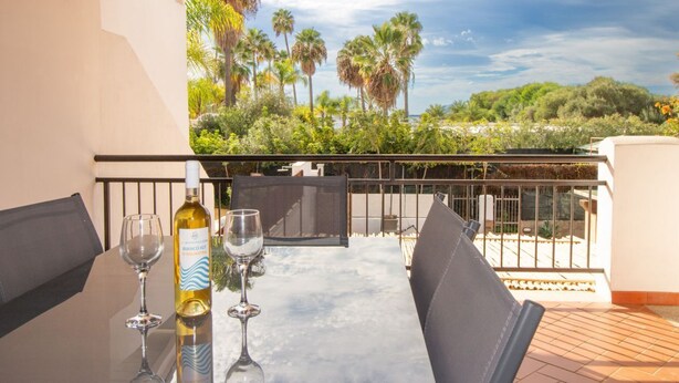 A table with two wine glasses and a bottle of wine, set against a backdrop of palm trees and a clear sky. - Waves Apartment, only 250m from the sea  (Tortolì)
