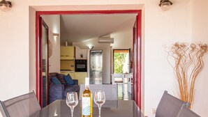 A dining area with a table set for two, a bottle of wine, and two glasses. The room has a modern design with a red-framed doorway leading to a kitchen and living area. - Waves Apartment, only 250m from the sea  (Tortolì)
