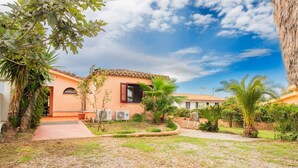 A two-story building with a tiled roof, surrounded by a well-maintained garden with palm trees and other greenery. - Waves Apartment, only 250m from the sea  (Tortolì)