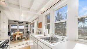 Een moderne keuken met witte kastjes, een groot raam en een eethoek met een houten tafel.