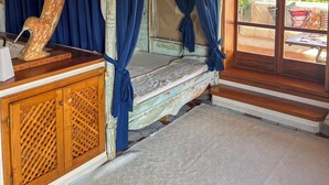 Una habitación rústica de madera con una cama bajo un dosel, un armario de madera y un gran ventanal con vistas a la vegetación.
