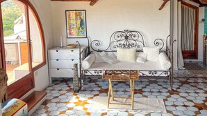 Una habitación acogedora con techo de madera, una cama con estructura metálica, pared blanca con un cuadro colorido y suelo de baldosas.