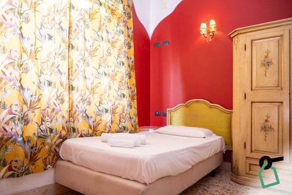 A hotel room with a bed, floral curtains, a wooden wardrobe, and a wall-mounted light fixture. - Hotiday Palermo Agostino (Palermo)