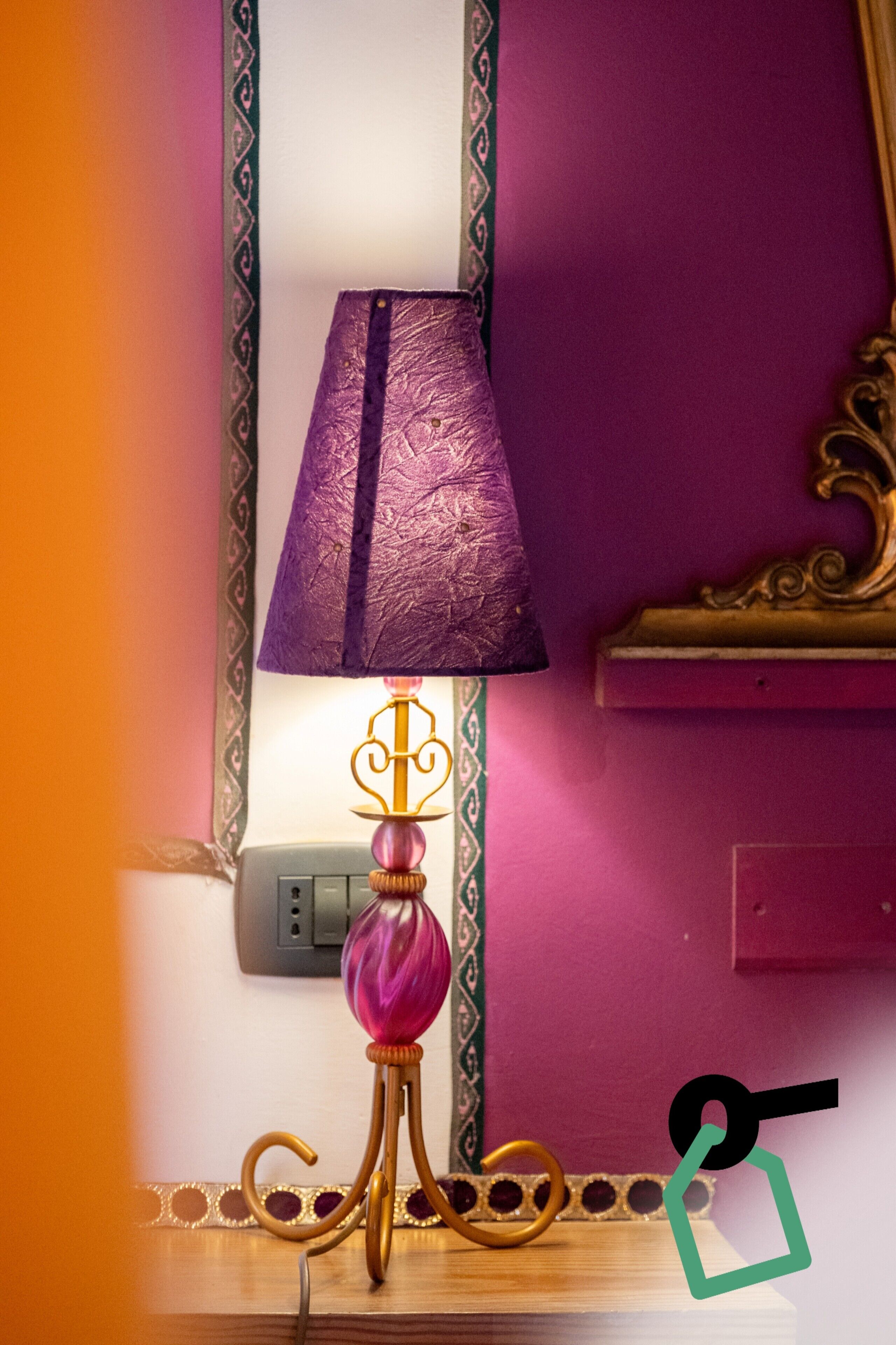 Eine violette Wand mit einer dekorativen Lampe und einer goldfarbenen Wandleuchte.