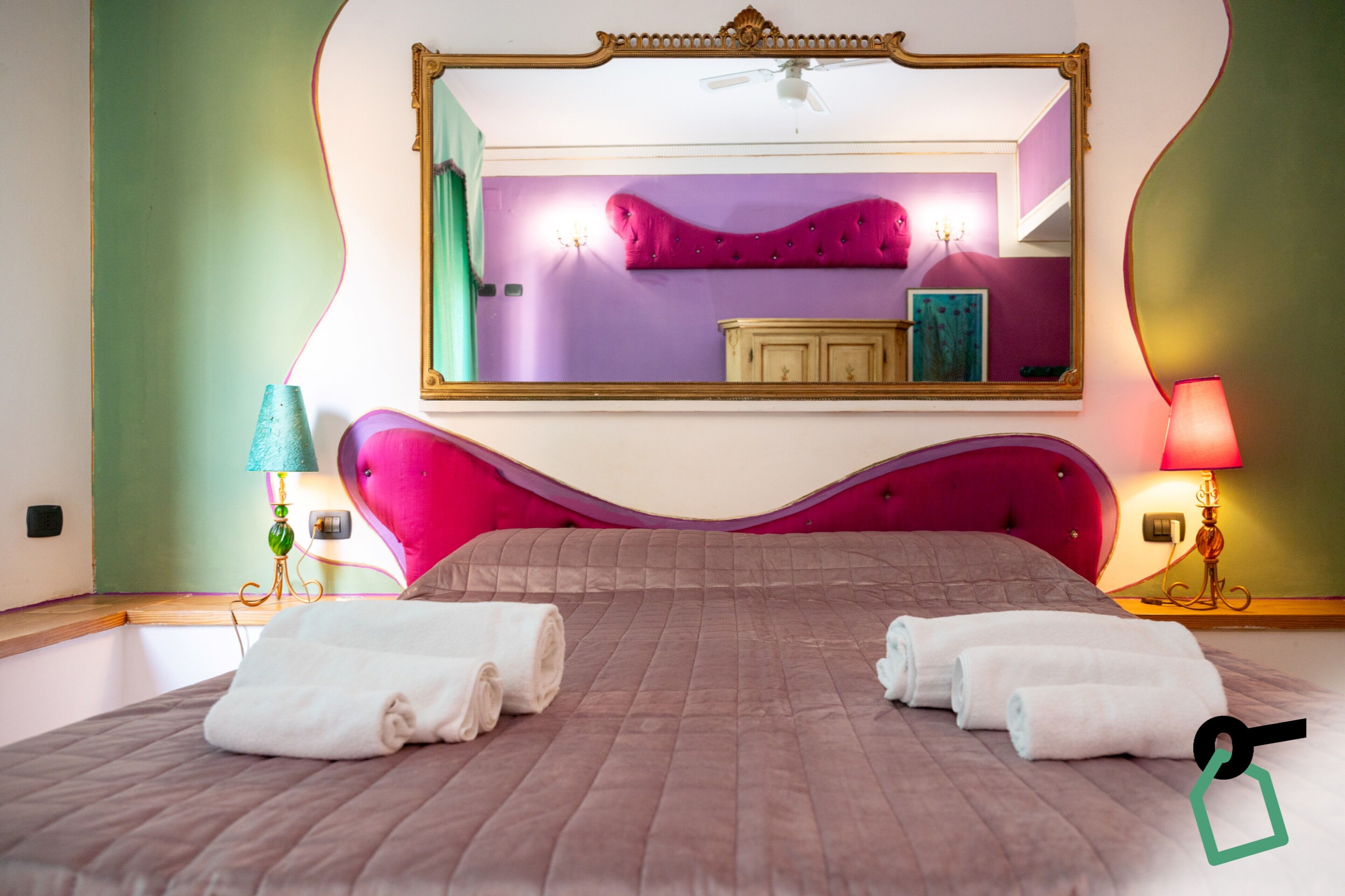 A hotel room with a large bed, two bedside lamps, a mirror, and a vanity with a mirror.