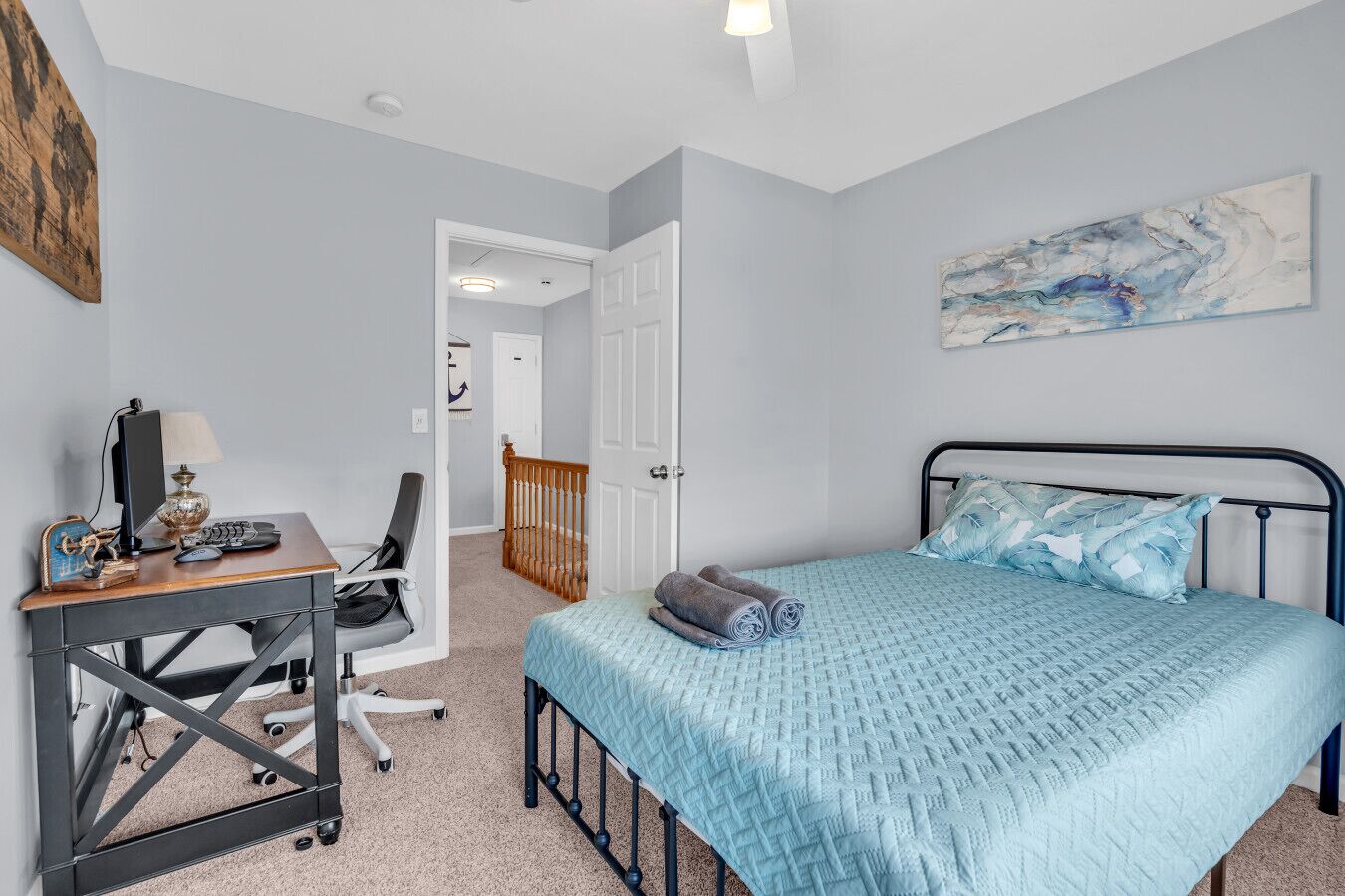 A bedroom with a bed, a desk with a computer, a chair, and a door leading to another room.
