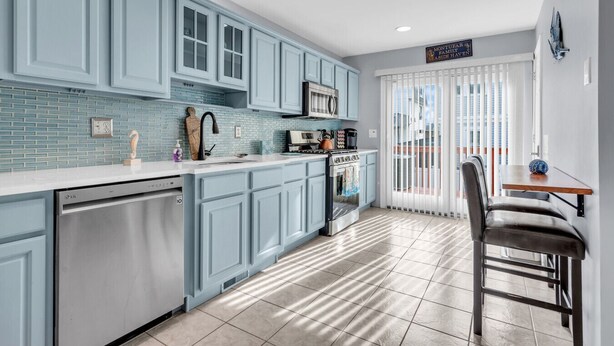 Una cocina moderna con armarios azul claro, encimera blanca y lavavajillas de acero inoxidable.