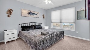 Un dormitorio con cama, mesita de noche, ventana con persianas y ventilador de techo.