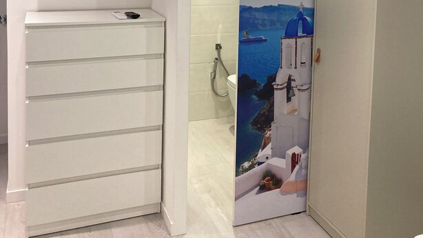 Een badkamer met een witte wastafel, een spiegel en een toilet. Er is een televisie aan de muur boven de wastafel bevestigd.