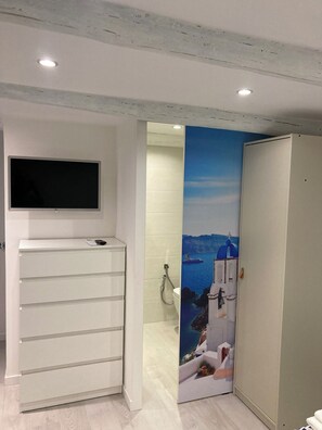 Ein Badezimmer mit einem weißen Waschbecken, einem Spiegel und einer Toilette. Ein Fernseher ist an der Wand über dem Waschbecken angebracht.