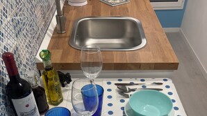 Een keuken met een gootsteen, een wijnfles, een glas en een blauw glas op een tafel met een tafelkleed met stippen.