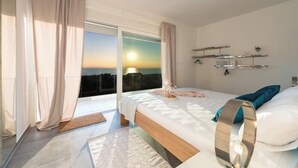 Ein modernes Schlafzimmer mit einem großen Bett, Blick auf den Sonnenuntergang und einem Balkon.