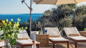 Eine Strandlounge mit Liegestühlen, einem Tisch mit einer Flasche und Blick aufs Meer.