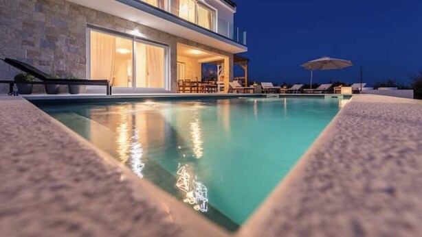 Ein modernes Haus mit Swimmingpool, Gartenmöbeln und einem gut beleuchteten Innenraum.