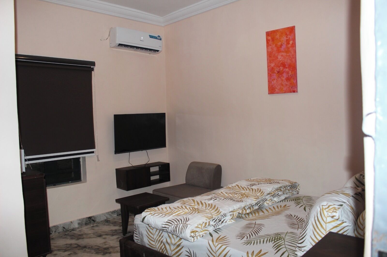 Ein Schlafzimmer mit einem Bett, einem Fernseher, einem Schreibtisch, einem Stuhl und einer Klimaanlage.