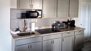 A modern kitchen with grey cabinets, a stainless steel sink, a black microwave, and a built-in toaster oven. - The Tolhouse Short or Long-Term (Essex)
