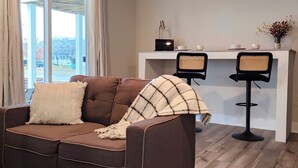 A modern living room with a brown sofa, white and plaid throw blankets, two black chairs, and a white console table with a lamp and a vase of flowers. - The Tolhouse Short or Long-Term (Essex)