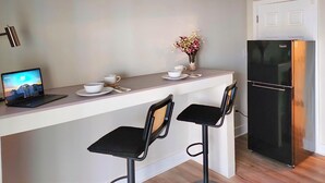 A compact kitchen with a refrigerator, two bar stools, a laptop on a counter, and a vase with flowers. - The Tolhouse Short or Long-Term (Essex)