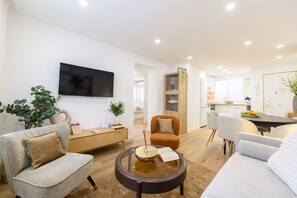 A modern living room with a sofa, armchair, and coffee table. There is a TV mounted on the wall and a kitchen area in the background. - M Gco69bd Apartamento de 3 Dormitorios (Madrid)