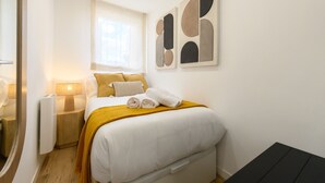 Une chambre d’hôtel avec un lit, une table de chevet avec une lampe, une fenêtre et des œuvres d’art abstraites accrochées au mur.