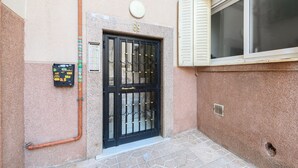 Une entrée d’immeuble avec un portail en métal noir, une plaque de numéro et un coffret de raccordement.