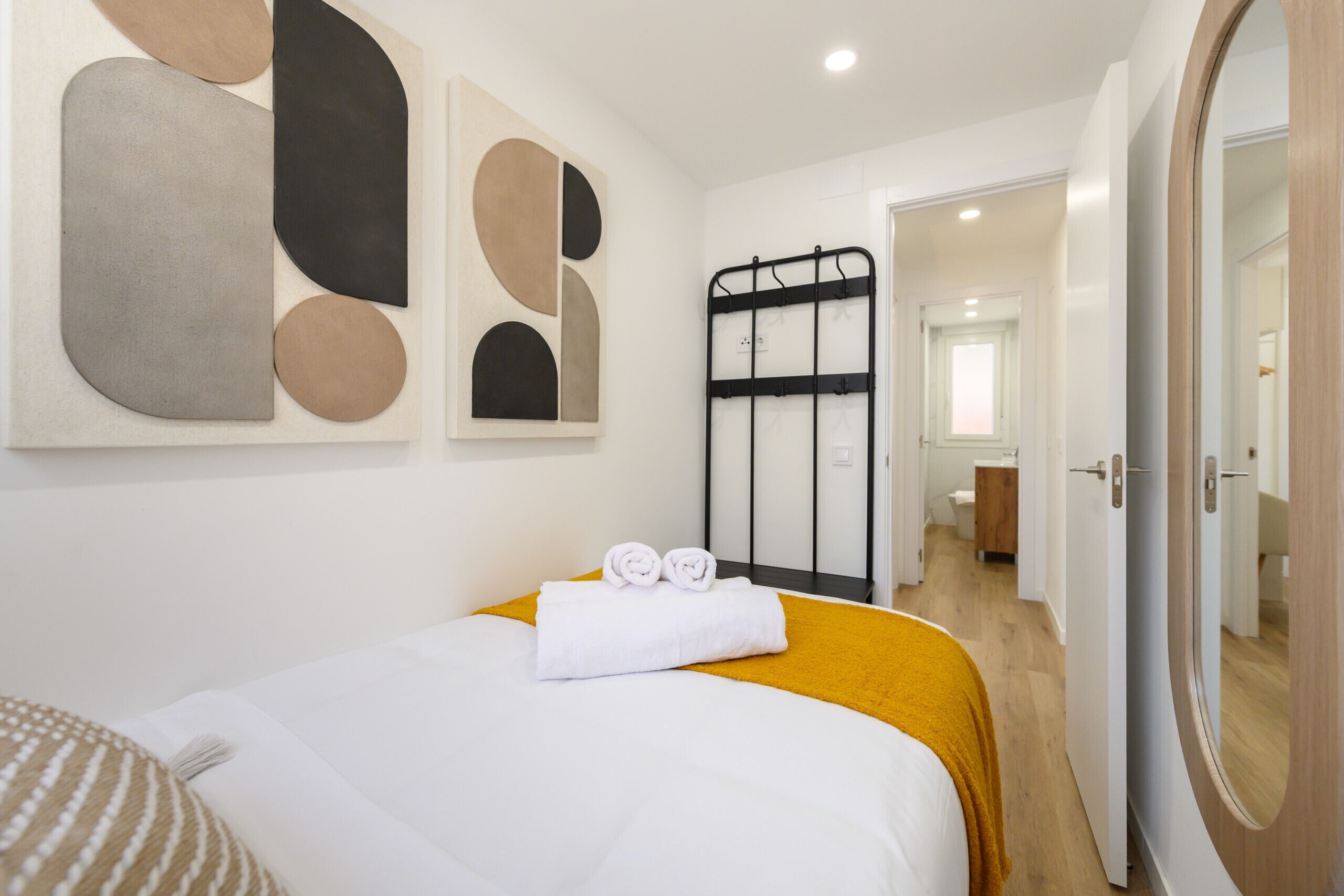 Una habitación de hotel con una cama, un cuadro abstracto grande, una reja de metal negro y una puerta de madera.