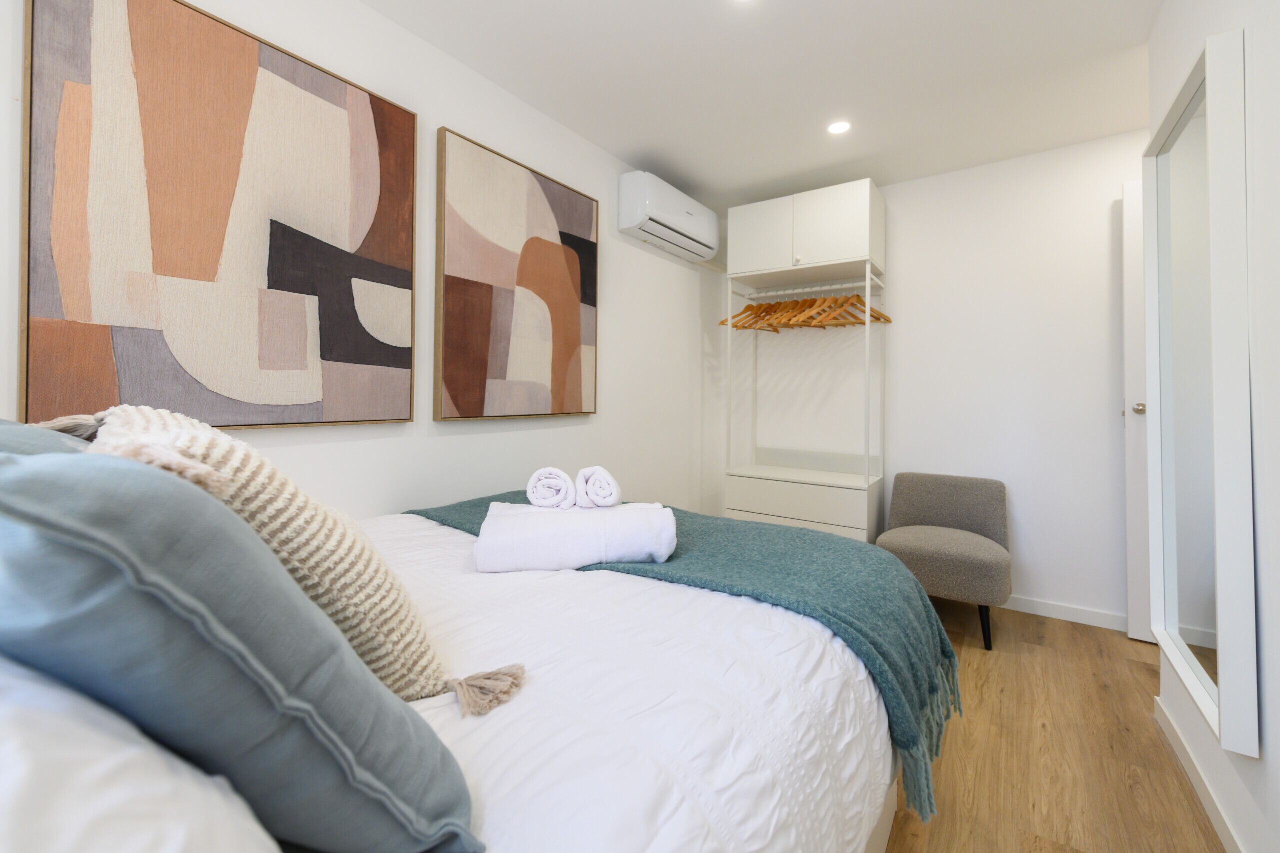 A bedroom with a bed, a chair, a wardrobe, and an air conditioning unit.