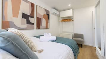 Un dormitorio con cama, una silla, armario y aire acondicionado.