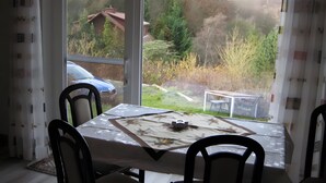 Ein Essbereich mit Tisch und Stühlen, Blick auf eine bewaldete Landschaft durch ein Fenster, und ein geparktes Auto draußen.