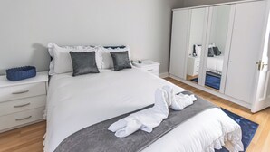 A neatly made bed with white linens and gray pillows, a bedside table with a blue basket, and a large wardrobe with a mirror. - POOL TABLE/ CINEMA ROOM/ WEEKLY DISCOUNTS (Glasgow)