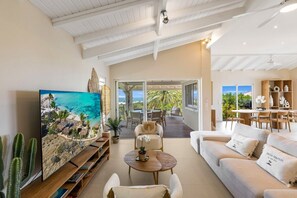 A spacious living room with a large painting, a sofa, a coffee table, and a dining area with chairs. - Villa Alanca • Vue Mer & Accès Plage à Pied (Orient Bay)