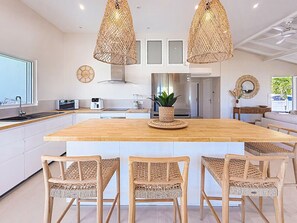 A modern kitchen with a large island, wooden chairs, and hanging wicker lamps.