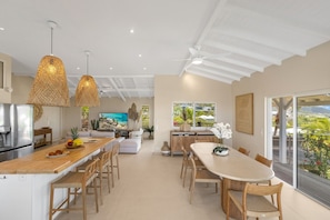 A modern kitchen with a dining area, large windows, and a view of the outdoors.