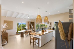 A modern kitchen with a central island, pendant lights, and a view of the outdoors.