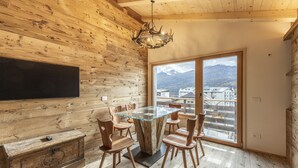 A wooden interior with a glass-top dining table, wooden chairs, a mounted television, and a view of buildings and mountains through a large window. - Poligrafica 1 House, quiet and comfortable (Cortina d´Ampezzo)