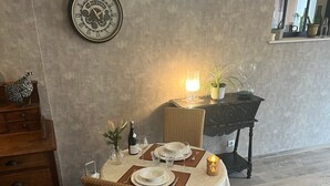 En matplats med ett runt bord för två personer, en dekorativ väggklocka, en takfläkt och ett fönster med utsikt.