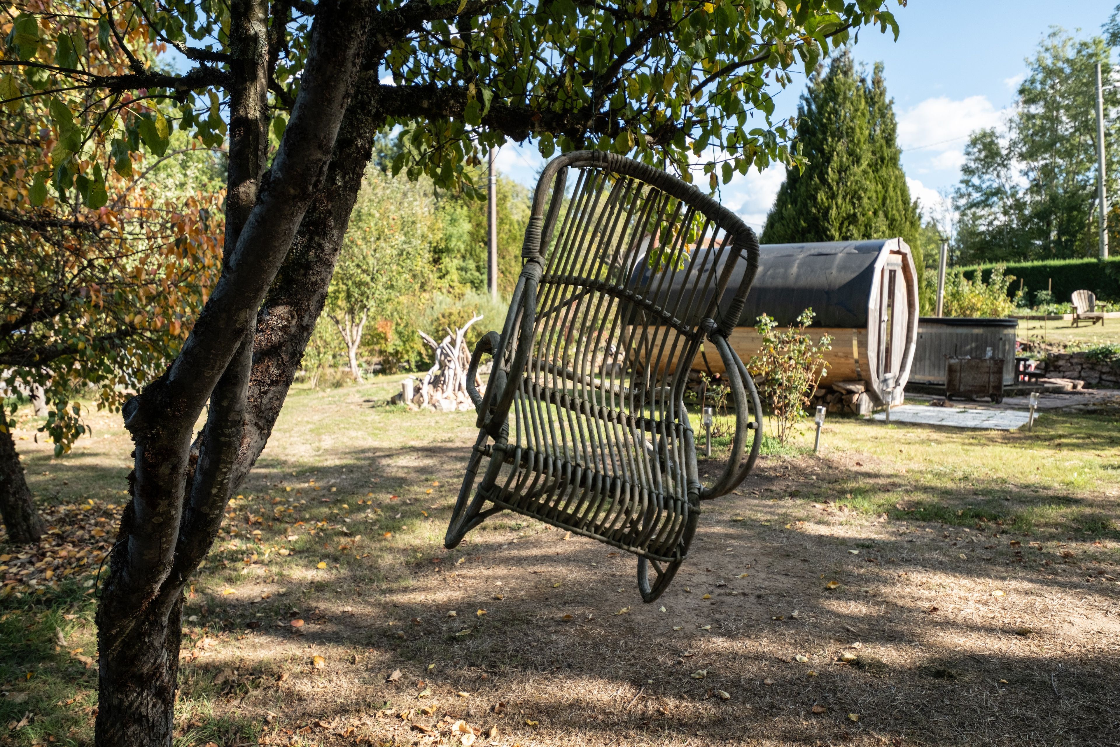 A rustic outdoor setting with a metal chair, a tree, and a cylindrical structure in the background.