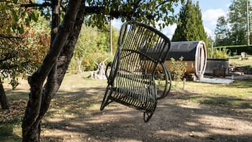 A rustic outdoor setting with a metal chair, a tree, and a cylindrical structure in the background.