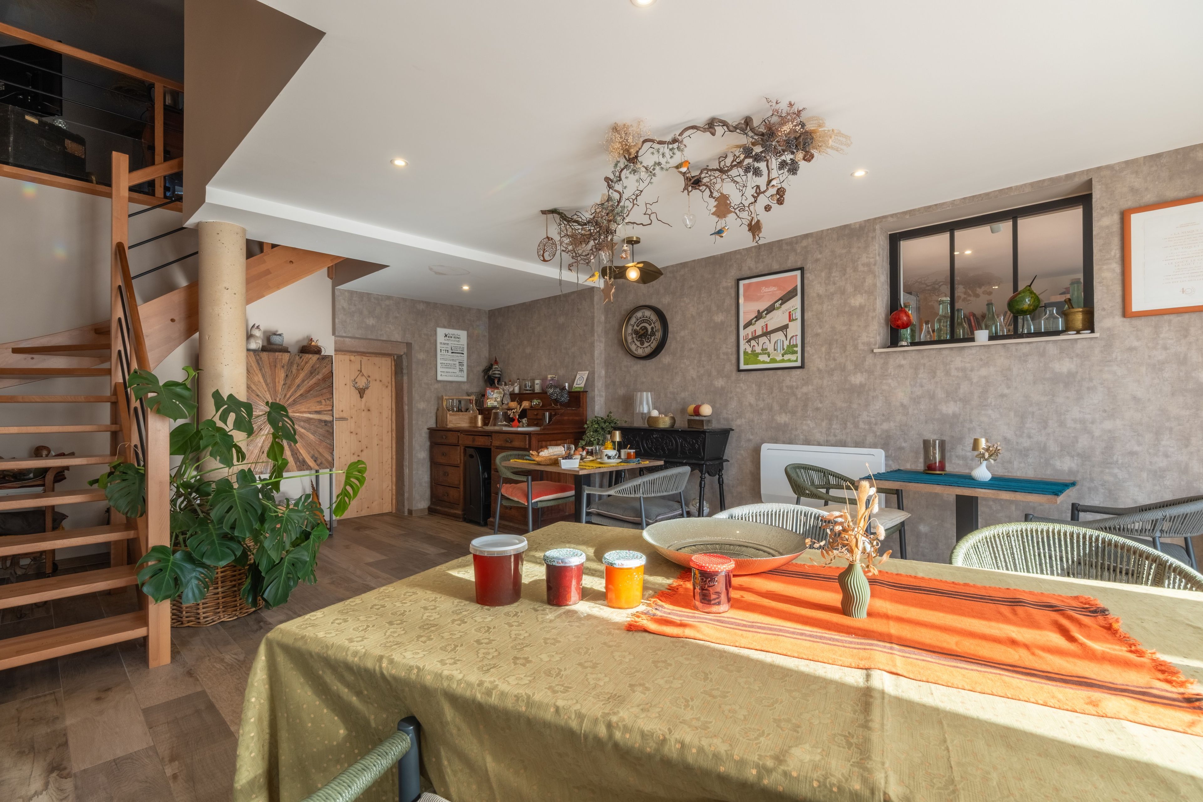 A dining area with a table set for four, a wooden staircase, and a kitchen in the background.