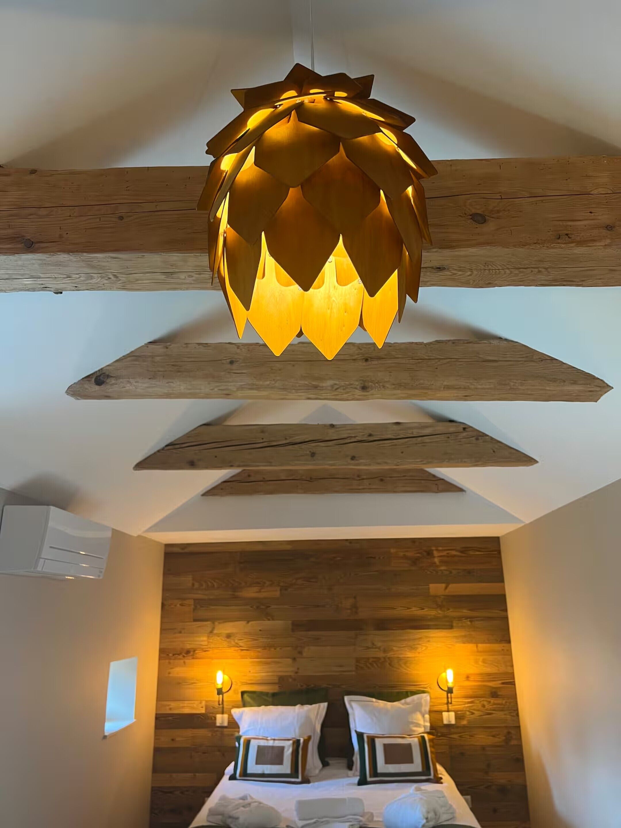 Ein Zimmer mit Holzboden, einer außergewöhnlichen Deckenleuchte, einem Bett mit Kissen und Wandlampen.