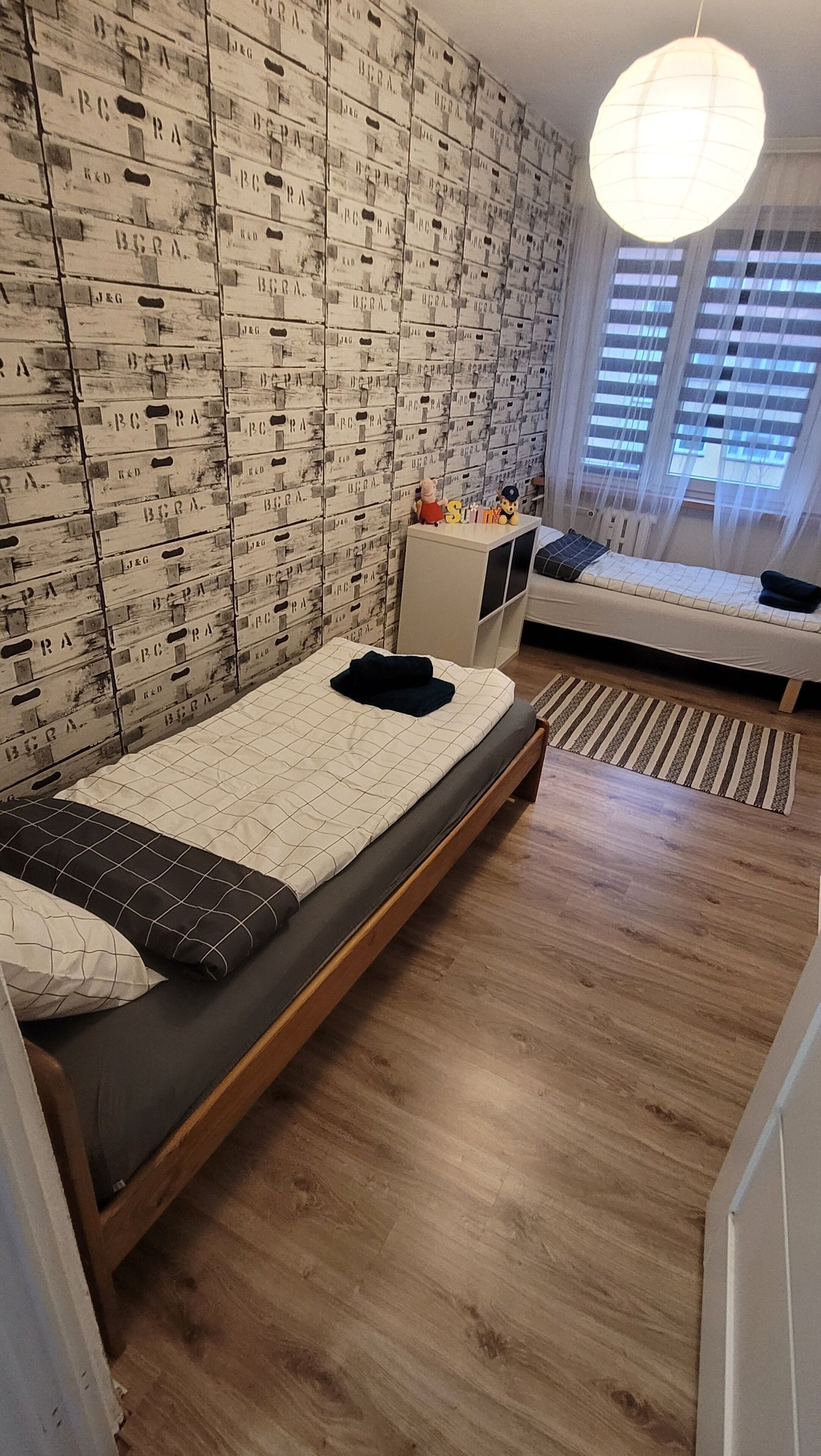 Una camera da letto con due letti, pavimento in legno e una parete decorata con scatole a motivi.