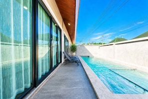 A modern hotel with a swimming pool, large windows, and a covered area with lounge chairs.